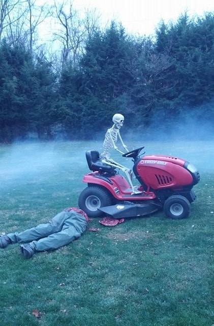 skeleton on lawnmower drives over corpse in Halloween fun decoration