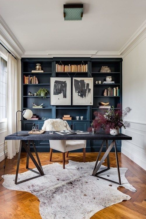 A cowhide rug, painted built ins, artwork and interesting writing table add depth and interest, and windows flood the space with natural light